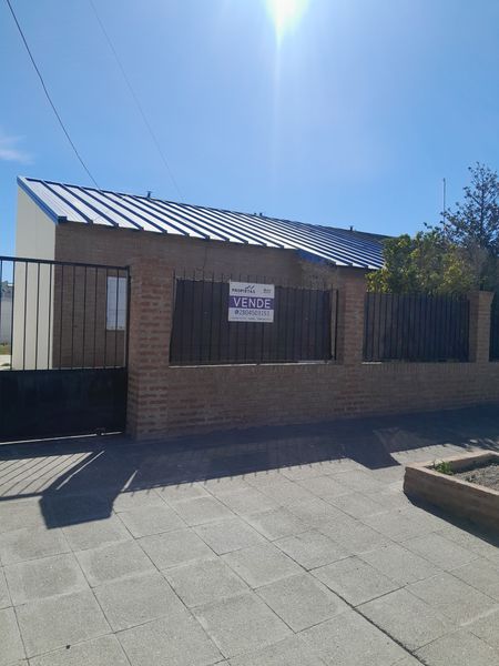 Frente de la casa: pared de ladrillo, reja y techo de chapa azul, con el cartel de venta de Propietas